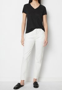 Svart kortärmad V-ringad skjorta i kombination med vita smala byxor och svarta loafers. Outfiten har en avslappnad och ledig passform samt en enkel design.