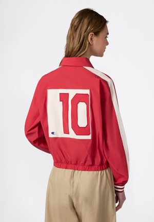 Donna vista di profilo che indossa una giacca rossa con strisce bianche e una grande toppa bianca con il numero 10 sul retro.