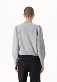 Grijze gebreide trui met een hoge halslijn, pofmouwen en een geribbelde zoom. Gecombineerd met zwarte jeans, wat eenvoud en comfort in het ontwerp laat zien.