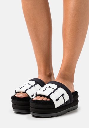 Černé platformové sandály s bílými polstrovanými pásky. Texturovaný povrch a měkké černé podšívání. Design s otevřenou špičkou, s robustní a silnou podešví.