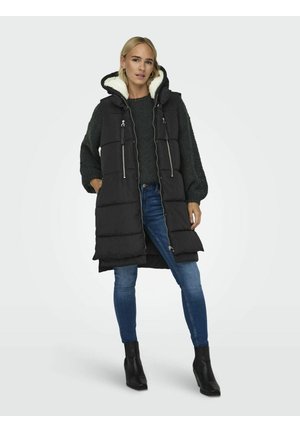 Doudoune noire avec capuche, avec une doublure blanche douce, deux poches zippées et un design long et structuré. Portée sur un pull sombre et un jean.
