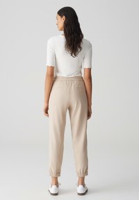 Beige joggerbroeken met elastische tailleband en omgeslagen boorden, gecombineerd met een witte aansluitende top met gekartelde mouwen. Witte sneakers gedragen.