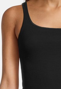 Czarny top na ramiączkach z dopasowanym krojem, miękką, prążkowaną fakturą i szerokimi ramiączkami. Materiał ma gładkie wykończenie i lekką elastyczność.
