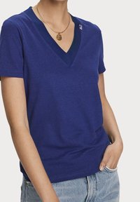 Mørkeblå v-hals t-shirt lavet af blødt stof, med en kontrasterende ribbet halsudskæring og en lille broderet detalje på venstre skulder.