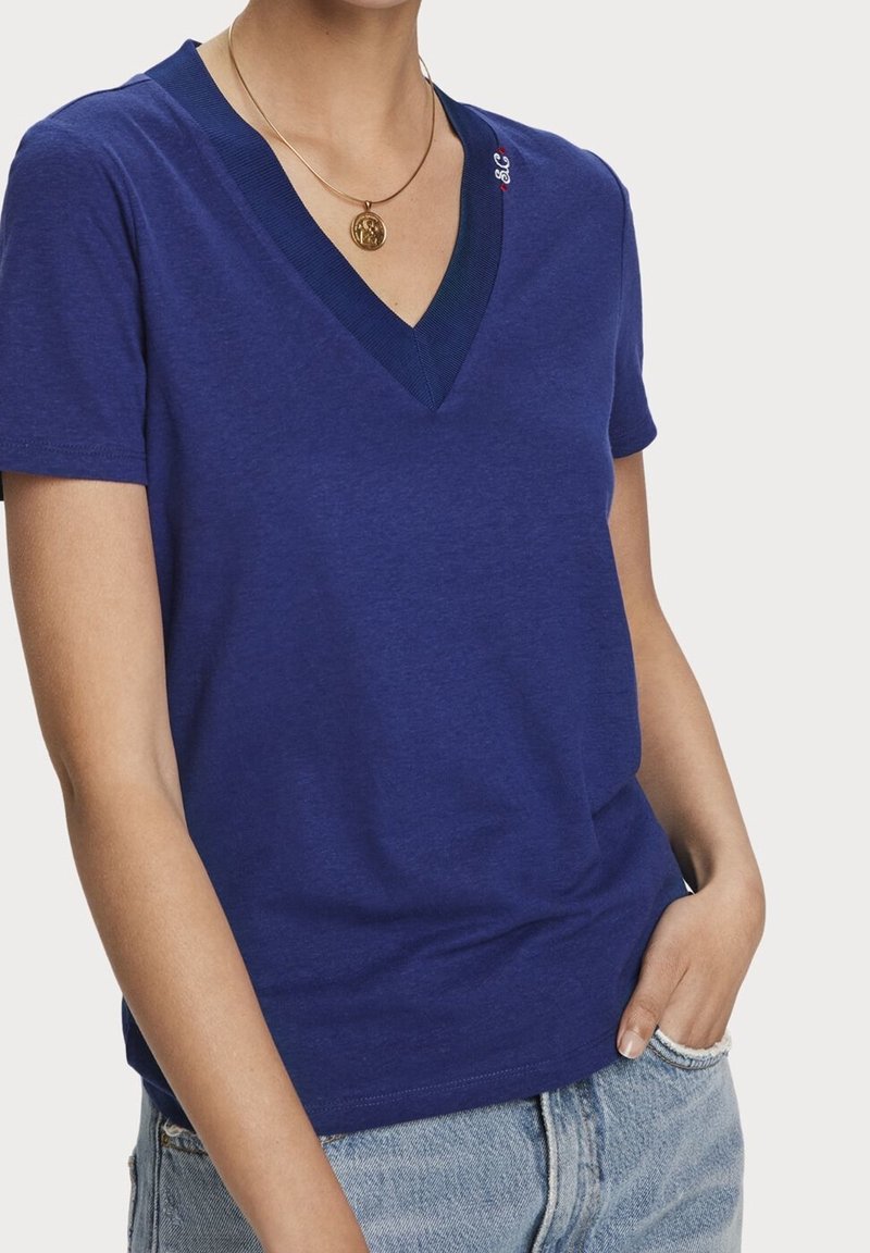 Mørkeblå v-hals t-shirt lavet af blødt stof, med en kontrasterende ribbet halsudskæring og en lille broderet detalje på venstre skulder.