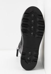 Bota negra con una parte superior de cuero texturizado, con una suela de goma. La suela tiene un patrón hexagonal para mayor agarre y una cremallera lateral para el cierre.