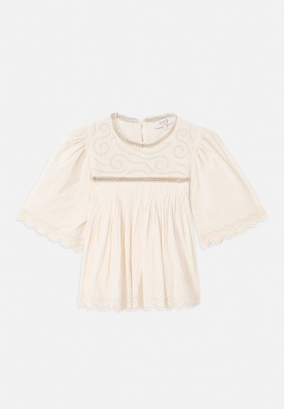 Cream blouse with wide sleeves, intricate embroidery on chest, scalloped lace trim on sleeves and hem, and pleated fabric below the chest.
