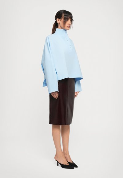 Light blue oversized top with a high collar and button placket, paired with a fitted burgundy leather skirt and black heeled mules.