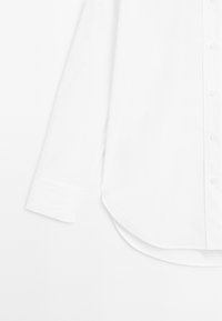 Hvid skjorte med lange ærmer og knapper, med afrundet kant, klassisk krave og manchetter med knapper. Glat stoftekstur uden mønstre eller dekorationer.