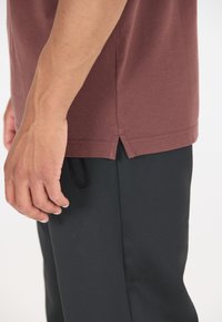 Bordeaux T-shirt i texturerat tyg med delad fåll, parat med svarta byxor med en liten ficka och elastisk dragsko.