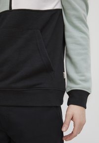 Felpa nera e verde menta con collo zip, tasca frontale e polsini a costine. Tessuto misto cotone con una sensazione di tessitura.