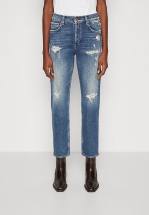 Blue denim jeans with distressed detailing, straight-cut design, whiskering, and faded patches. Worn with brown ankle boots.