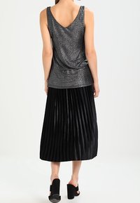 Schwarzer plissierter Midirock mit glänzendem, strukturiertem Finish; kombiniert mit einem eng anliegenden, glitzernden grauen Tanktop mit drapiertem Rücken und breiten Trägern.