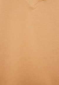 Suéter de cuello en V hecho de una tela suave y lisa en un color durazno claro; cuenta con una textura sutil y un diseño limpio y minimalista.