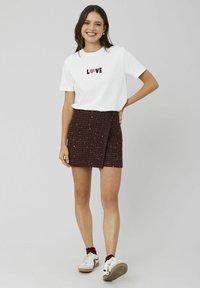 T-shirt blanc à manches courtes avec le texte "LOVE", associé à une mini-jupe texturée bordeaux. Le modèle porte des baskets blanches avec des accents bordeaux.