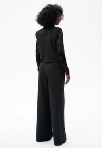 Czarny dopasowany kombinezon z usztywnianą górą i przeźroczystymi, haftowanymi długimi rękawami. Szerokie nogawki i gładka faktura.