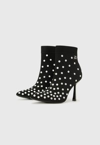 Black ankle boots with white polka dots, featuring a knitted upper, pointed toe, and a stiletto heel. Accented with a logo detail.