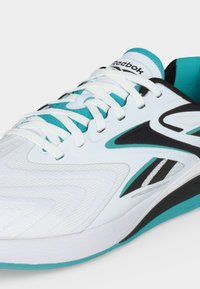 Λευκό και τιρκουάζ αθλητικό παπούτσι Reebok με μαύρες λεπτομέρειες, λευκά κορδόνια και υφασμάτινη υφή στην περιοχή των δαχτύλων.