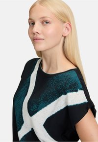 Svart och turkos kortärmad topp med ett iögonfallande geometriskt mönster i vitt och texturerad tyg med rund halsringning och avslappnad passform.