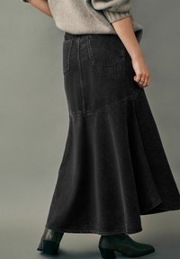 Sort denim maxiskirt med en flæsednedre kant, der har to baglommer og kontraststikninger. Stylet med mørke hæklede ankelstøvler.