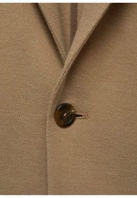 Tissu de blazer marron avec un tissage texturé, doté d'une fermeture à un bouton marron et de deux revers crantés.