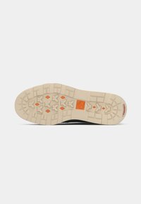 Black shoe sole with a textured beige rubber traction pattern, featuring an orange accent in the center and branding near the heel.