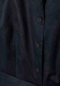 Vêtement bleu marine à la texture lisse, présentant des motifs cachemire embossés complexes et des boutons noirs sur le devant.