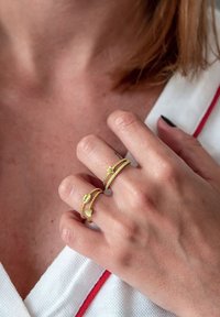 Zelta toņa gredzeni ar savītiem bandām, kuru rotājumi ir: sirds, zvaigzne un dārgakmeņa formas elements. Valkāti uz rokas ar īsiem nagiem.