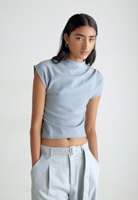 Light gray fitted top with cap sleeves and a high neckline; smooth, stretchy fabric; paired with high-waisted, light gray trousers.