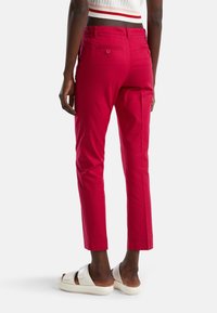 Röda bomullsbyxor med en figurnära passform, bakfickor med knappar och ankellängd, tillsammans med ljusa skidsandaler.