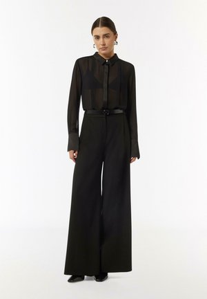 Black sheer long-sleeve blouse with a button-down collar paired with black high-waisted wide-leg trousers and a fitted belt. Smooth textures.