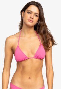 Růžový bikiny top s trojúhelníkovým designem, tenkými ramínky a nahrnutým materiálem uprostřed. Hladký povrch bez vzorů.
