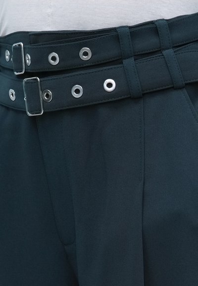 Sötétzöld szövet nadrág, dupla övdesignnal, ezüst hardware-ral és szemekkel. Sima textúra, igényes elülső plissékkel.