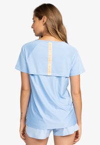 Lichtblauwe sport T-shirt met een contrasterende verticale logoband aan de achterkant. Korte mouwen en een losse pasvorm met een gladde textuur.