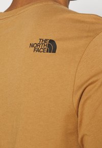 Braunes Baumwoll-T-Shirt mit Rundhalsausschnitt und kurzen Ärmeln. Auf dem oberen Rücken befindet sich ein schwarzes Logo von "The North Face".