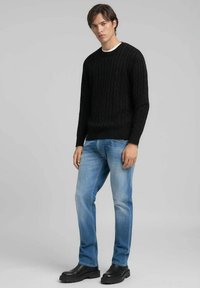 Pull en maille noire avec motif torsadé, col rond et poignets côtelés. Porté avec un jean bleu clair et des bottines noires.
