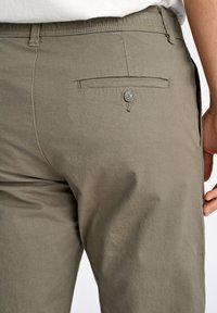 Pantalons vert olive avec une texture lisse, présentant une poche arrière avec une fermeture à bouton et un motif de coutures subtil le long des coutures.