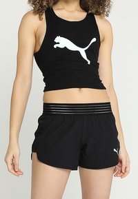 Débardeur noir côtelé avec un logo Puma blanc, associé à un short noir doté d'une ceinture élastique rayée et de poches latérales.