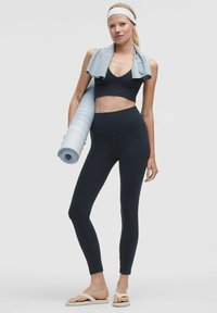 Fekete sportos crop top és magas derekú leggings, egy világoskék edzőszőnyeggel párosítva. Kiegészítők között szerepel egy világoskék törölköző és fejpánt.