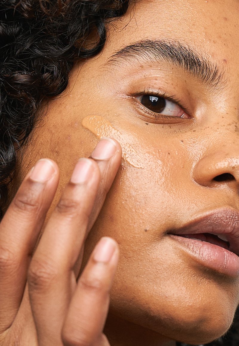 Flytende foundation blir påført en lys brun hudtone. Teksturen ser jevn ut, med en kremet konsistens og en subtil glød.