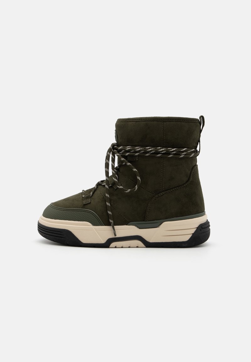 Olive green suede boot with a padded collar, black and white patterned laces, chunky white sole, and textured rubber accents.