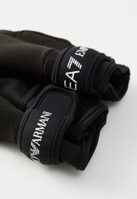 Black gloves made of a textured fabric with elastic cuffs. White embroidered branding on the cuffs. Feature a snug, fitted design.