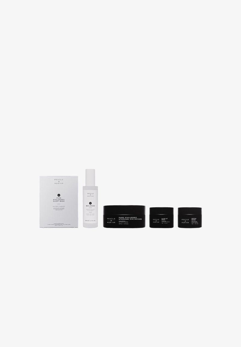 Ensemble de soins de la peau comprenant un flacon pulvérisateur blanc, des pots noirs de différentes tailles et une boîte blanche. Texte sur les contenants en blanc et noir.