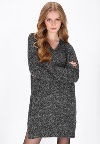 Sötét szürke, túlméretezett pulóverruha V-nyakkivágással, hosszú ujjal és textúrázott kötött mintázattal; az oldalsó hasítékok könnyű mozgást biztosítanak.