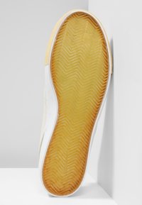 Semelle de chaussure avec une semelle inférieure en caoutchouc jaune texturée présentant un motif en zigzag, encadrée par un bord en caoutchouc blanc. Design propre et simple.