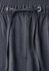 Donkergrijze, lichte stof met een elastische tailleband en een trekkoord. Bevat een zijzak en heeft een gladde textuur.