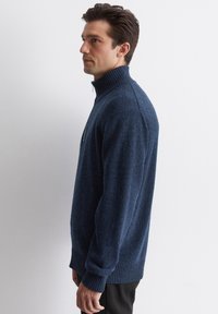 Dunkelblauer Strickpullover mit einem gerippten hohen Kragen, strukturiertem Muster und langen Ärmeln. Subtile gesprenkelte Gestaltung im gesamten Stoff.
