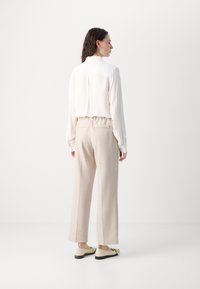 Leichte, langärmelige Bluse in Creme mit vertikalen Falten und einem abgerundeten Kragen, kombiniert mit beigen, hochtaillierten Hosen, die eine entspannte Passform zeigen.