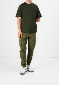 T-shirt in cotone verde oliva e pantaloni cargo, caratterizzati da una vestibilità dritta e polsini affusolati. Abbinati a scarpe da ginnastica bianche con dettagli neri.