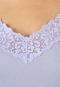 Top sin mangas de color púrpura claro con un delicado borde de encaje alrededor del escote; textura de canalé visible debajo del detalle de encaje.